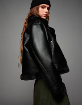 Person wearing a black leather jacket and black beanie against a gray background